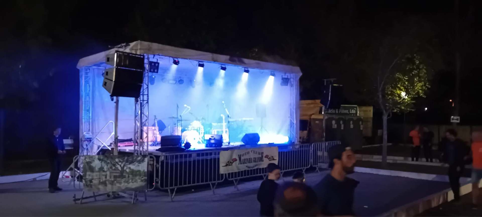 Palco coberto com iluminação azul e som profissional em evento noturno